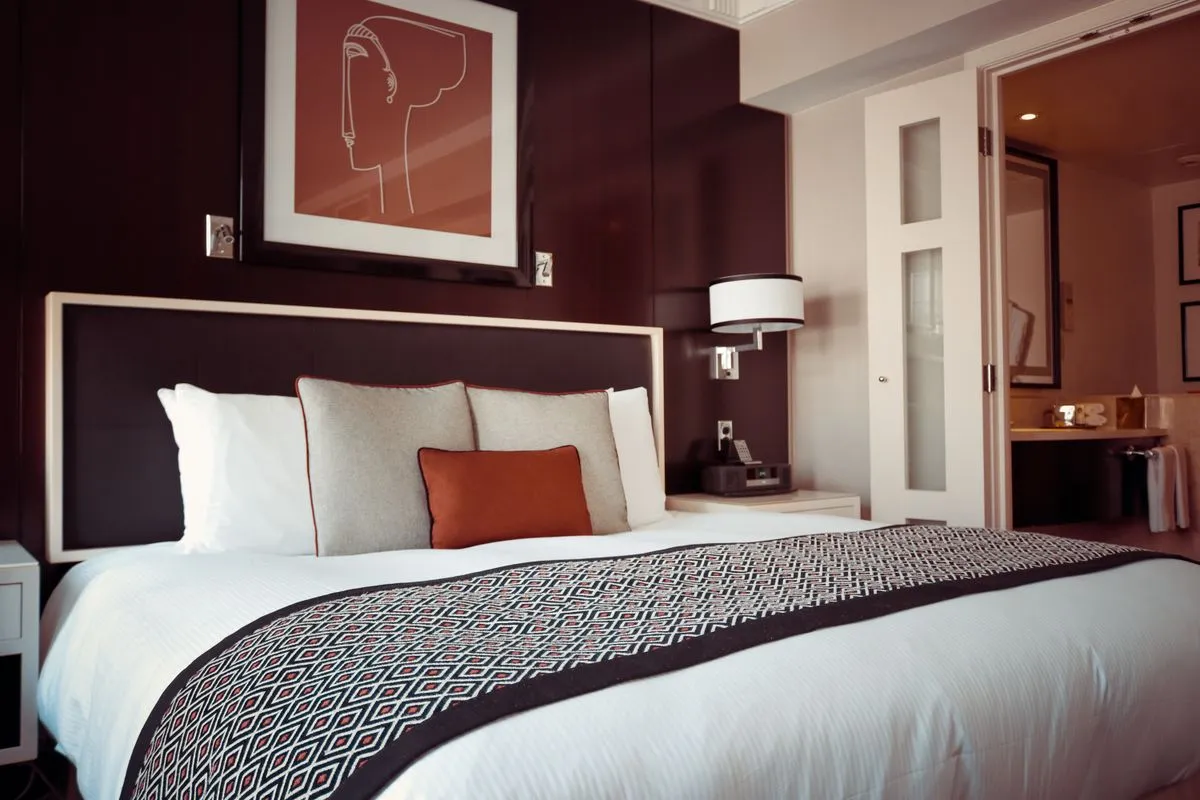 Cleaner checking a mattress headboard and box spring for pest signs while preparing a short-term rental bedroom