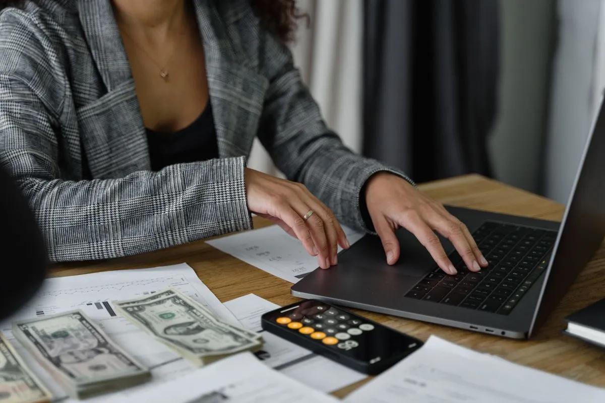Host working on a laptop with a calculator and banknotes to recalculate Airbnb nightly prices after the new host-only service fee