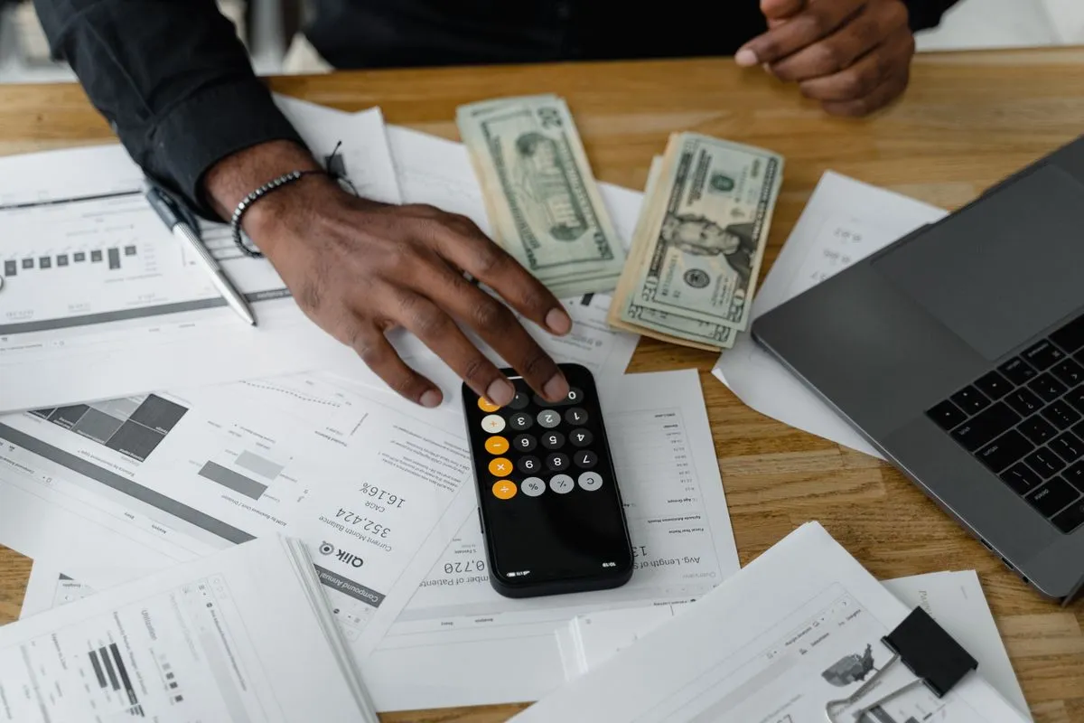 Host calculating rental income with a calculator, banknotes and a laptop after Vrbo's move to a 12% host commission
