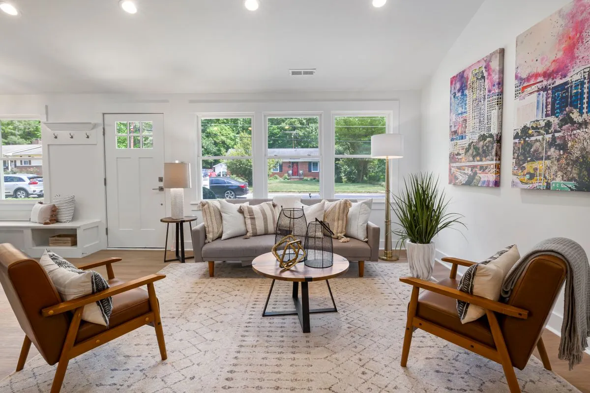 Salon lumineux avec canapé gris, deux fauteuils en cuir et grandes fenêtres, photographié en grand angle pour une annonce de location